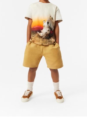 Light beige t-shirt with a colorful rhinoceros graphic, paired with yellow shorts. Brown sneakers, white socks. Casual, comfortable design.