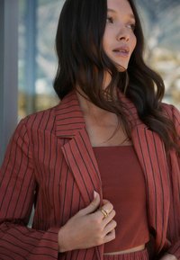 Blazer couleur rouille avec des rayures verticales, associé à un haut assorti. Présente des revers structurés et une coupe décontractée. Accent de bague en or.