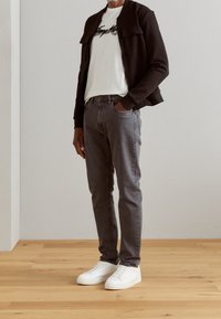 Chaqueta bomber negra sobre una camiseta blanca, jeans gris ajustados y zapatillas blancas. Diseño simple con patrones y acentos mínimos.