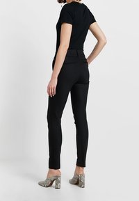 Czarne dopasowane spodnie o gładkiej teksturze i tylnych kieszeniach; w połączeniu z jasnoszarymi szpilkami w wężowy wzór.