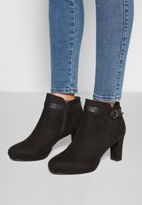 Mustat nilkkurit, joissa on mokkanahkaa, pyöreä kärki, vetoketjClosure, koristeellinen hihna, jossa on pyöreä yksityiskohta, ja kohtuullinen lohkokorko.