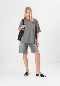 Pilka per didelė t-shirt su mėlynu logotipu, derinama su pilkais džinsiniais šortais ir juodomis blokinėmis kulniuko sandalais. Juoda petneša su diržu.