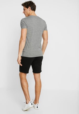 Grijze, nauwsluitende t-shirt van zacht materiaal, gecombineerd met zwarte shorts. Witte sportschoenen met zwarte accenten. Schoon, minimalistisch ontwerp.
