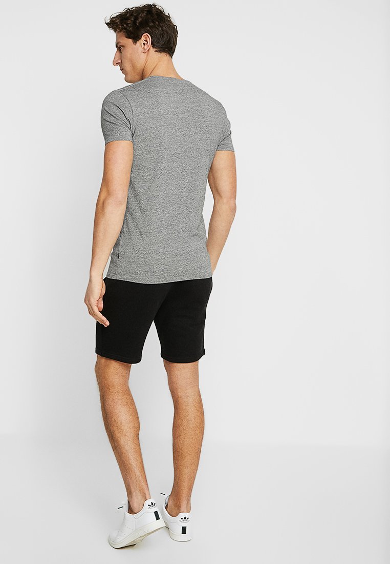 Grau passendes T-Shirt aus weichem Material, kombiniert mit schwarzen Shorts. Weiße Sportschuhe mit schwarzen Akzenten. Sauberes, minimalistisches Design.