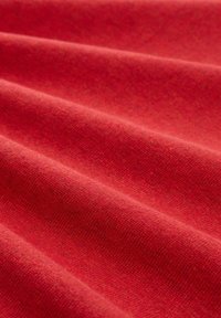 Tessuto rosso drappeggiato in pieghe morbide, che mostra una texture liscia e un colore uniforme con un sottile motivo intrecciato.