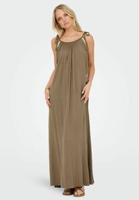 Robe maxi vert olive avec des bretelles ajustables à nouer, un décolleté froncé et une texture légère. Associée à des sandales plates marron.