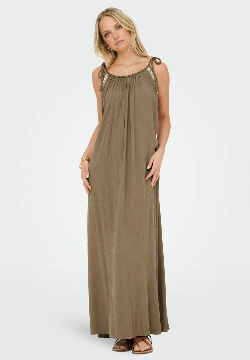 Robe maxi vert olive avec des bretelles ajustables à nouer, un décolleté froncé et une texture légère. Associée à des sandales plates marron.