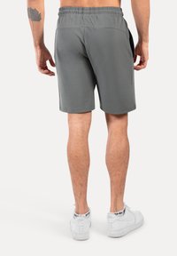 Grijze sportshorts met een elastische tailleband, zijzakken en een gladde textuur, getoond van de achterkant, gecombineerd met witte sneakers.