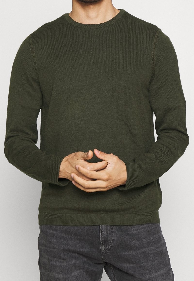 Un pull vert foncé avec un col rond, des poignets et un ourlet côtelés, et une coupe ajustée, fabriqué en un matériau tricoté doux et extensible.
