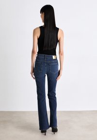 Blå denim flared jeans med mid-rise liv, som har baklommer og en rektangulær gullhardwaredetalj på livet.