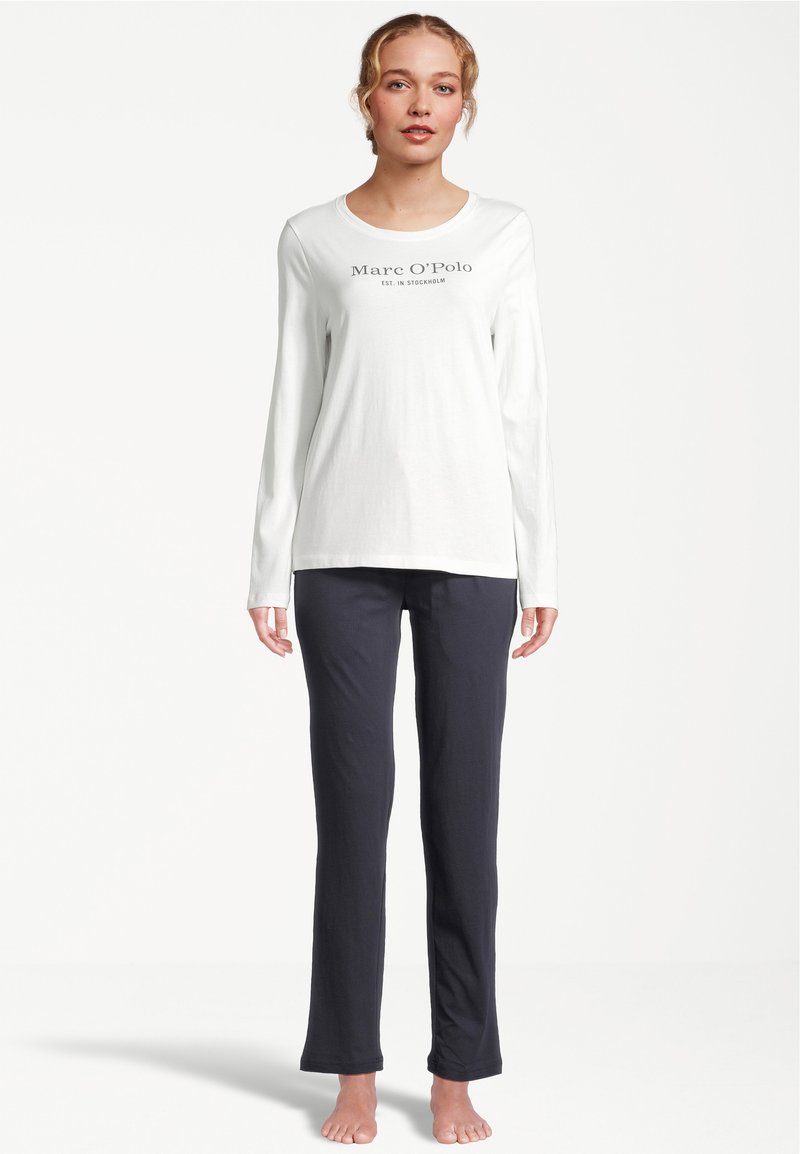 Witte lange mouw top met de tekst "Marc O'Polo", gecombineerd met donkerblauwe broek. Beide kledingstukken hebben een eenvoudige, ontspannen pasvorm en zachte textuur.