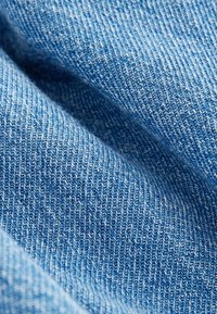 Gros plan sur un tissu denim bleu texturé avec un motif de tissage diagonal visible et des plis souples créant des ombres.