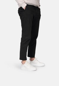 Chinos negros de corte slim y longitud hasta el tobillo, combinados con zapatillas blancas que presentan una superficie lisa y texturizada, además de un diseño con cordones.