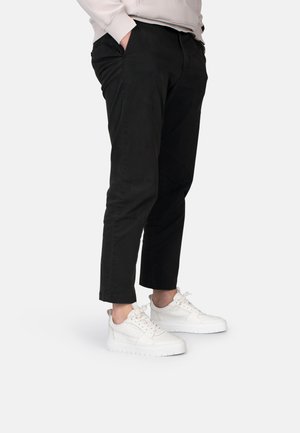 Chinos neri con vestibilità slim e lunghezza alla caviglia, abbinati a sneakers bianche con una superficie liscia e testurizzata e design con lacci.