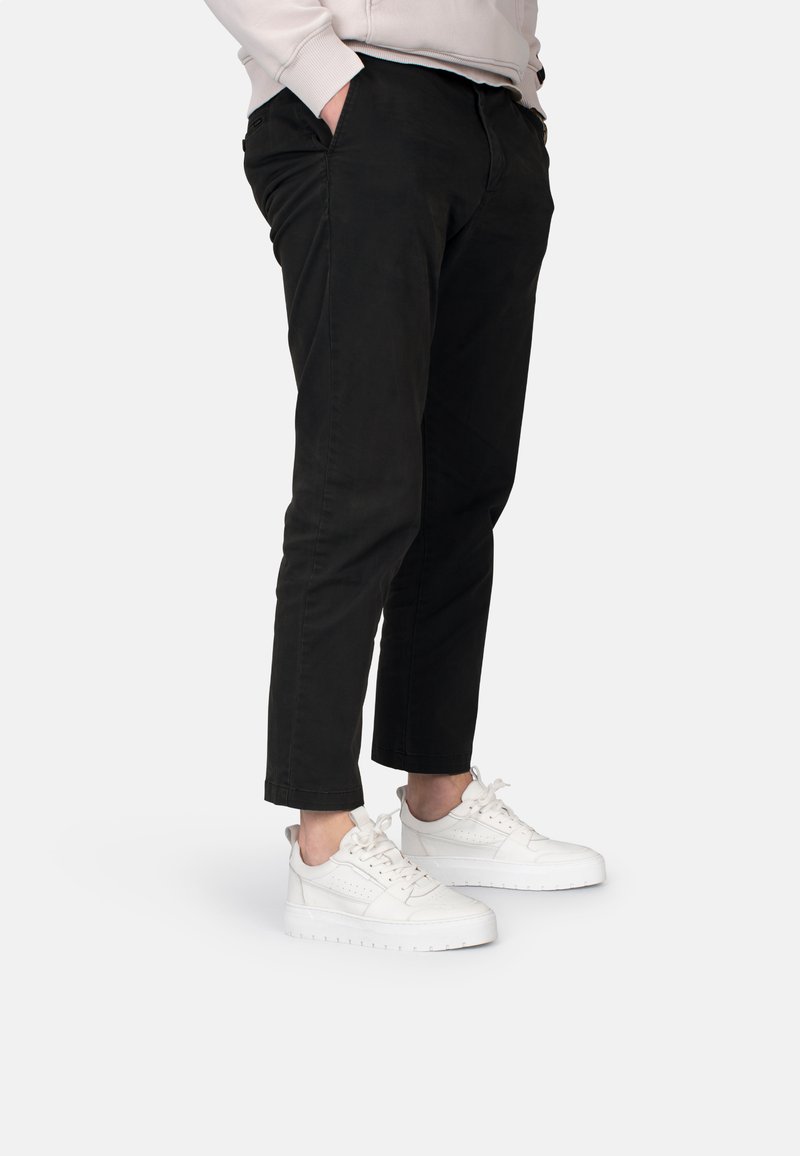 Chinos negros de corte slim y longitud hasta el tobillo, combinados con zapatillas blancas que presentan una superficie lisa y texturizada, además de un diseño con cordones.