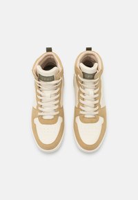 Beige-weiße High-Top-Sneaker aus Leder mit gepolstertem Schaft, runder Zehenpartie, weißen Schnürsenkeln und einem kleinen grünen Etikett auf der Rückseite.