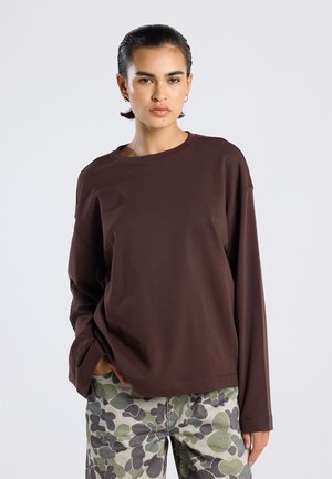 Bruine lange mouw shirt van zacht materiaal met een ronde halslijn en een relaxte pasvorm, gecombineerd met groen en grijs geblokte broek met bladmotieven.