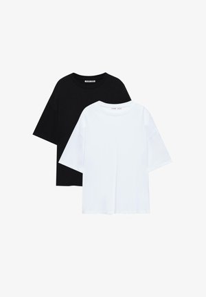 Two plain oversized crew neck T-shirts, one black behind one white, laid flat on a white background.