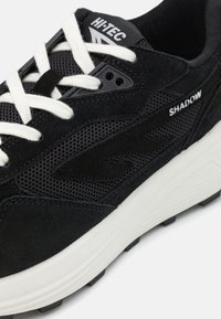 Schwarzer Sportschuh mit Obermaterial aus Mesh und Veloursleder, weißen Schnürsenkeln, gepolstertem Schaft und kontrastierender weißer Zwischensohle. Verfügt über Logo- und Textergänzungen.