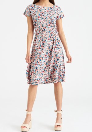Woman wearing a knee-length, short-sleeve floral dress with a cinched waist and ruffle hem, paired with beige wedge sandals with ankle straps.