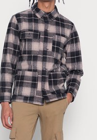 Károvaná bunda v černé, šedé a béžové barvě s límečkem, zapínáním na knoflíky, dvěma předními kapsami a mírně vypasovaným střihem.
