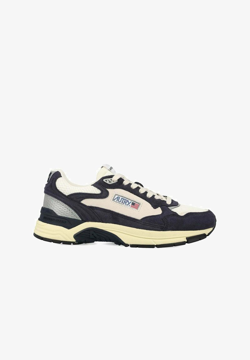 Baskets combinant une tige en suède bleu marine foncé et en mesh crème, avec une semelle épaisse et des accents de panneaux argentés. Logo AUTRY affiché.