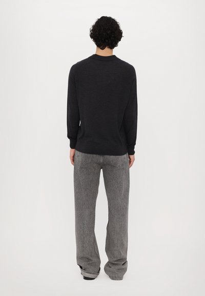 Chemise à manches longues gris foncé en matériau doux, avec un col rond et des poignets côtelés, associée à un jean large gris clair.