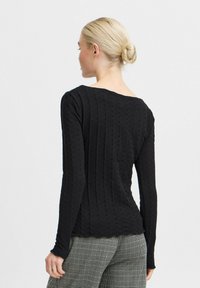 Top negru cu mâneci lungi, cu un design texturat și striat și un decolteu rotund pe spate. Are mâneci ajustate și o linie de tiv curbată.