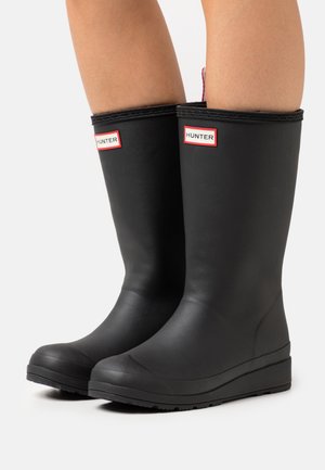 Bottes de pluie en caoutchouc noir avec une finition texturée, arborant une étiquette de marque. Le design comprend une semelle légèrement surélevée et un bout arrondi.