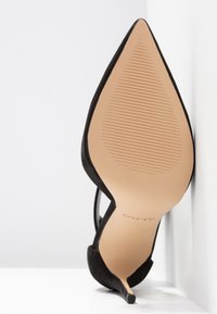 Chaussure à talon aiguilles noire à bout pointu montrée par la semelle avec une semelle extérieure beige rainurée et le nom de la marque "ALDO" visible.