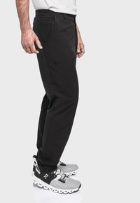 Schwarze Sportleggings mit einem eleganten Design, Reißverschlusstasche und glatter Textur, kombiniert mit grau-schwarzen Sneakers.