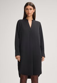 Zwart shirtjurk gemaakt van zacht materiaal, met een V-hals, lange mouwen en zijsplitten voor bewegingsvrijheid. Aansluitende pasvorm.