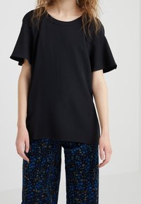 Czarna bluzka z krótkim rękawem o szerokim dekolcie i gładkiej teksturze. W zestawie z wzorzystymi niebiesko-czarnymi spodniami w kwiaty, prezentującymi żywe kolory.