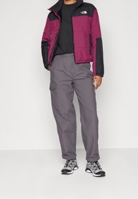 Maroon og sort puffjakke med lynlås, parret med grå cargo-bukser og grå sneakers med sorte accenter. Flad stofstruktur.