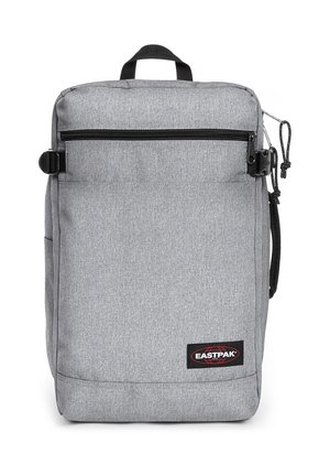Mochila de tela gris con forma rectangular, que incluye un bolsillo frontal con cremallera, un asa superior y una cremallera lateral. Logotipo de Eastpak visible.