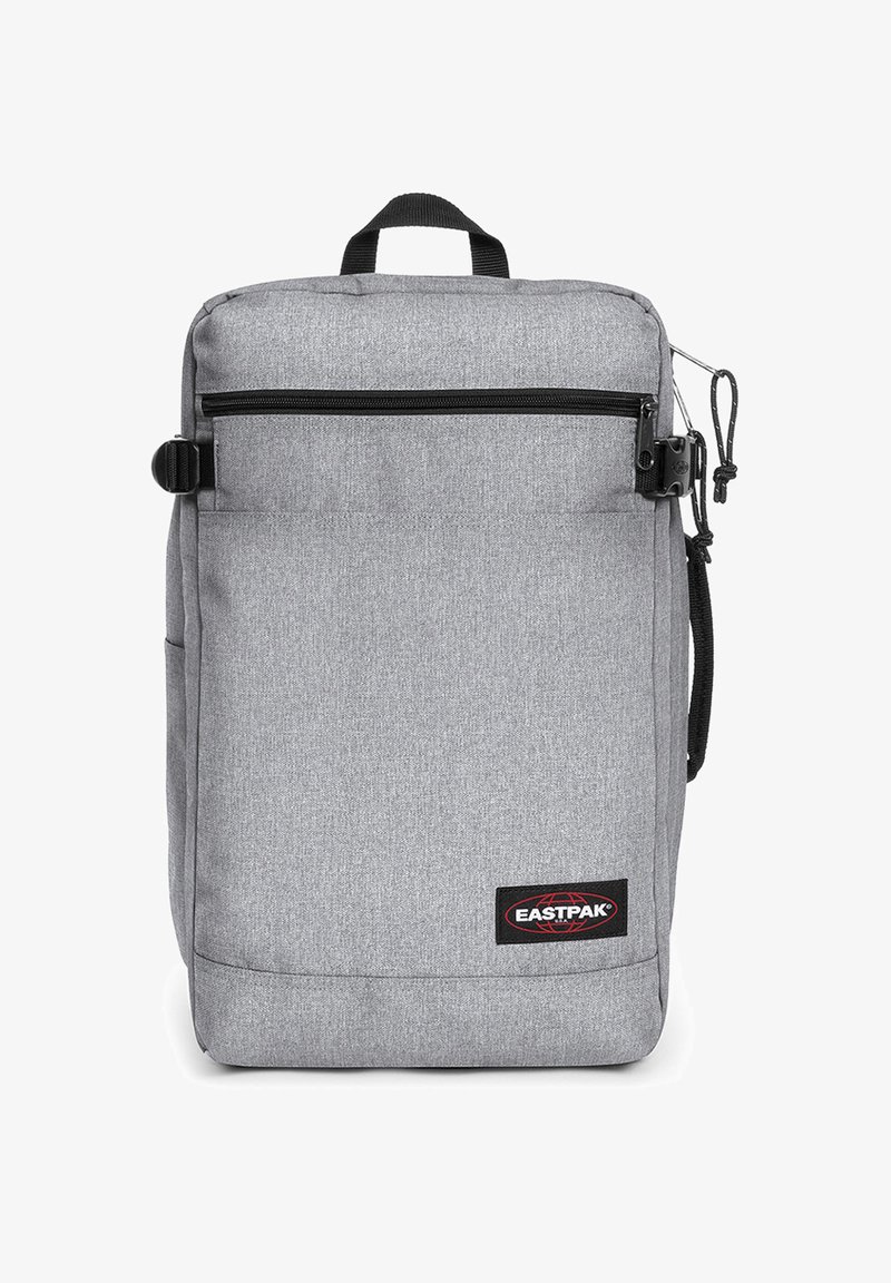 Szary materiałowy plecak o prostokątnym kształcie, z przednią kieszenią na zamek, górnym uchwytem i bocznym zamkiem. Logo Eastpak widoczne.