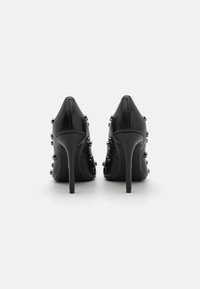 Chaussures à talons hauts en cuir noir avec bouts pointus, ornées de clous argentés sur les côtés et de talons aiguilles fins. Texture lisse.