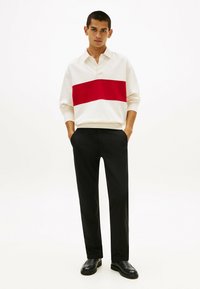 Weißes Langarmpolo mit horizontalem rotem Streifen, kombiniert mit schwarzen geraden Hosen und schwarzen Schuhen. Schlichtes Design und weicher Stoff.