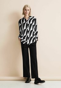 Camicia a maniche lunghe bianca e nera con motivo ondulato, con bottoni davanti, abbinata a pantaloni neri a gamba larga e scarpe nere stringate.