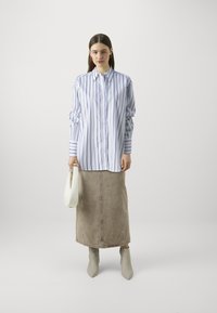 Blue and white striped button-up shirt, beige denim skirt, gray ankle boots, and a white handbag. Simple design with contrasting colors.