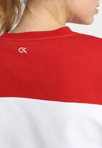 Red and white cotton T-shirt featuring a color-block design with a white section at the bottom and a small logo in white at the neck.