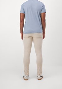 Light blue short-sleeve t-shirt paired with beige fitted pants and black-and-white sneakers. Smooth fabric, simple design, no visible patterns.