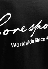 Čierna tkanina s bielym textom „Lone sho“ kurzívou a „Worldwide Since“ tučným písmom.