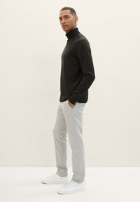 Zwarte coltrui gecombineerd met lichtgrijze slim-fit broek en witte sneakers, gepresenteerd tegen een neutrale achtergrond.