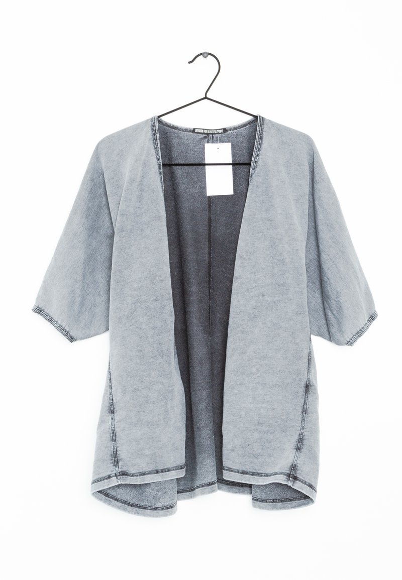 Cardigan gris clair ouvert devant avec manches courtes suspendu à un cintre noir, montrant des coutures visibles et une étiquette de prix blanche.