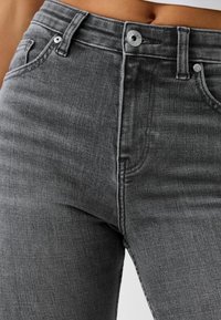 Vaqueros de mezclilla gris con un diseño ajustado, que cuentan con una cintura alta, estilo de cinco bolsillos y detalles de herrajes metálicos en la cintura.