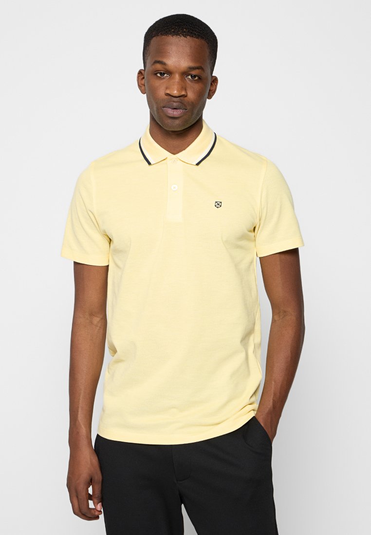 Camiseta polo amarilla de manga corta, con un cuello con ribete negro y un pequeño logo en el pecho. La tela parece suave y ligera.