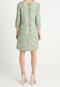 Blommig klänning i mintgrön tyg med trekvartsärmar, bakre nyckelhålsstängning och en lös passform, med rosa och blå blommönster.