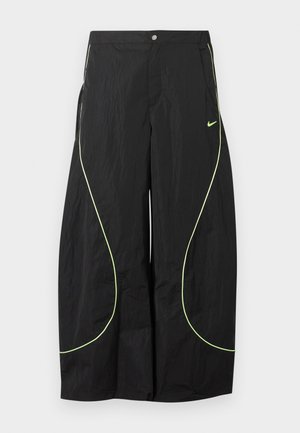 Sorte Nike bukser med brede ben, med neon-grøn buet piping og lille Nike swoosh-logo på højre lår, knap- og lynlåslukning i taljen.