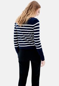 Pull à rayures bleu marine et blanc à manches longues avec une silhouette ajustée. Texture lisse et ourlet arrondi, associé à un pantalon noir.